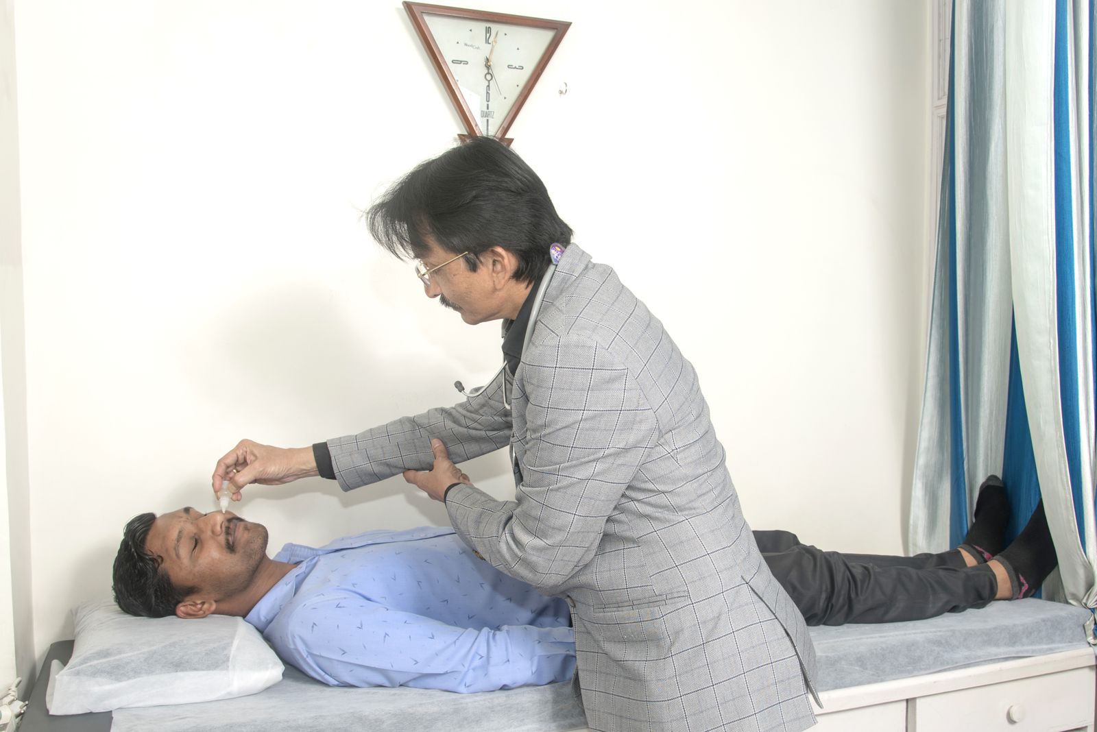 Dr. Gujarathi administering herbal nasal drops to a patient on the treatment bed